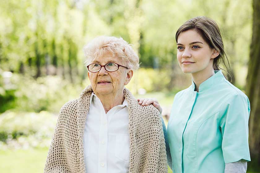 happy senior woman and helpful caregiver nursing home