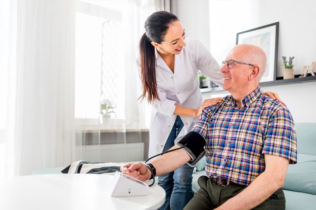 nurse visiting senior male at home doing blood pressure measurement