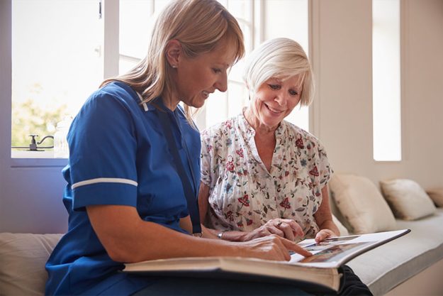 senior woman sitting looking photo album with nurse