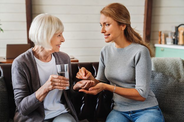 senior woman taking pills her daughter while holding glass water