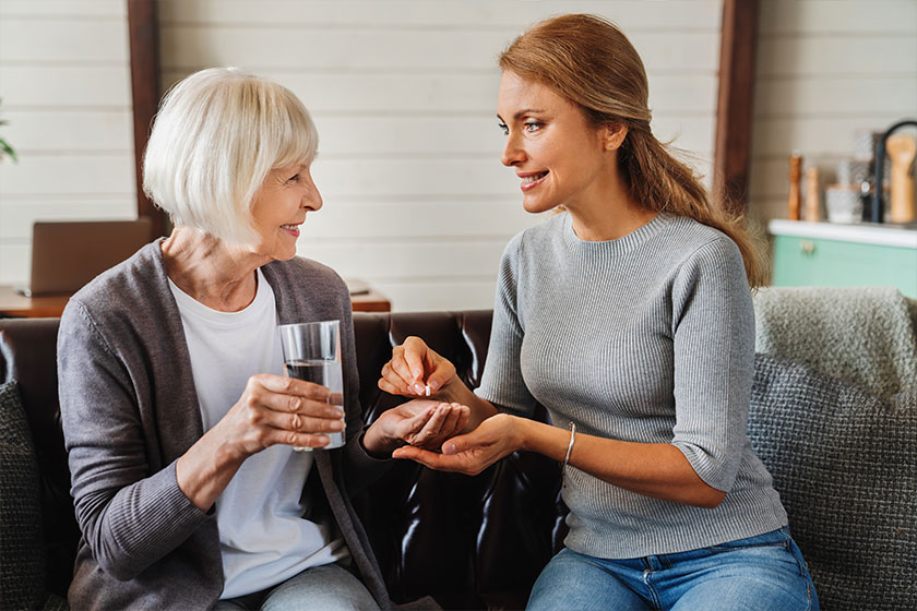 senior woman taking pills her daughter while holding glass water senior woman taking pills her daughter while holding glass water