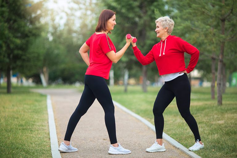 two beautiful adult women doing sports dumbbells summer park
