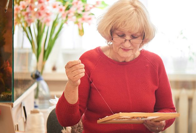 elderly woman red sweater embroidering while sitting home