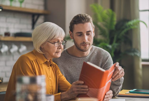 elegant good looking grey haired woman and her son reading a book