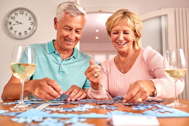 senior retired couple sitting table home glass wine doing jigsaw