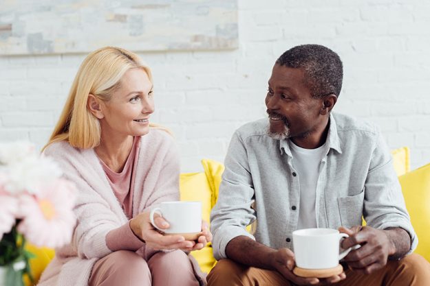 smiling mature woman sitting sofa african american man drinking coffee 