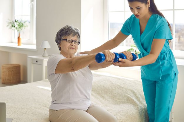 physiotherapist or home care nurse helping senior woman do rehabilitation exercise