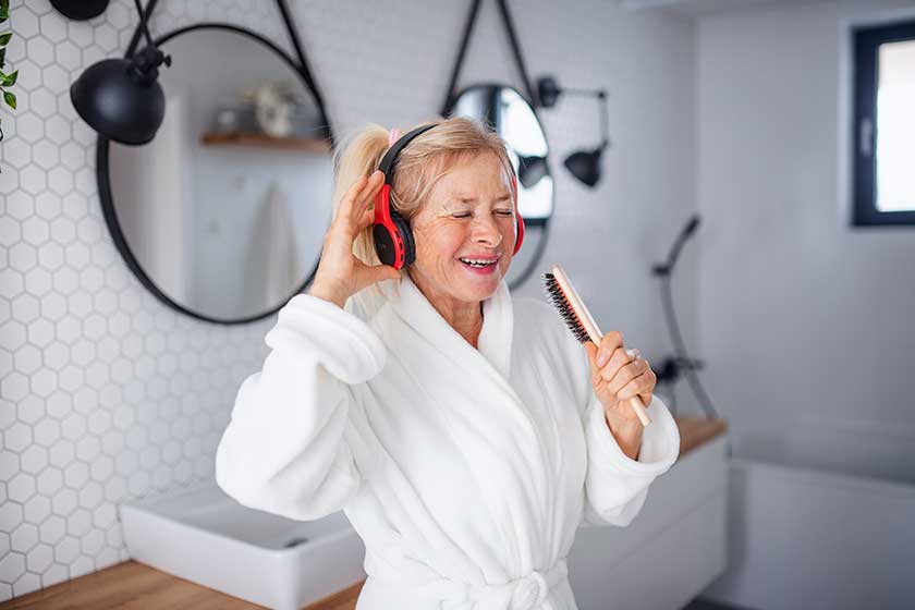 portrait of senior woman with headphones and bathrobe indoors at home