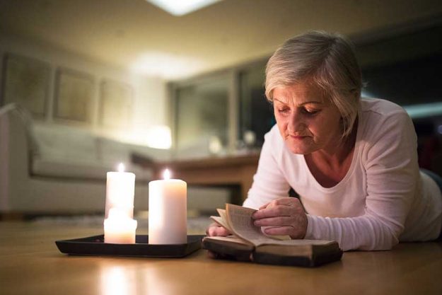 senior woman reading bible burning candles next to her