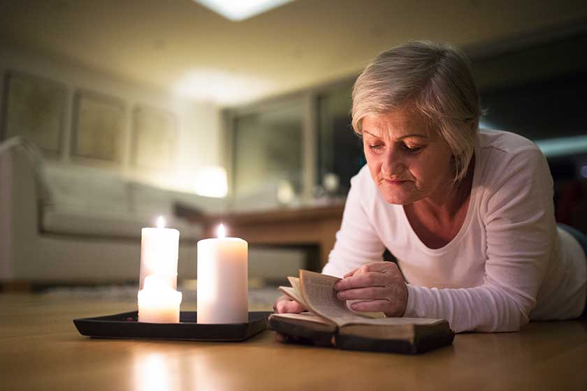 senior woman reading bible burning candles next to her