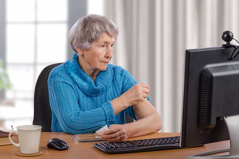 elderly woman gives an intramuscular injection in front of computer monitor