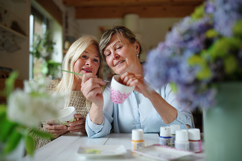 happy senior woman artist teaching her friend how to paint cermaic cup artcraft concept