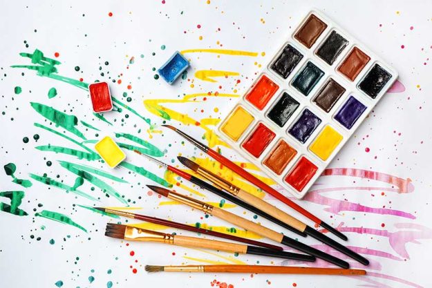 plastic palette with colorful paints and brushes on light background top view