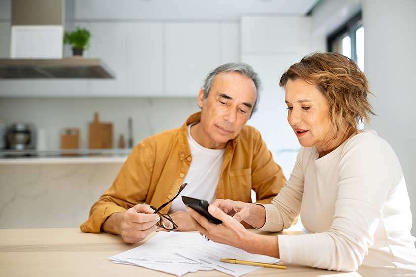 senior couple sitting kitchen papers bills using calculator husband wife