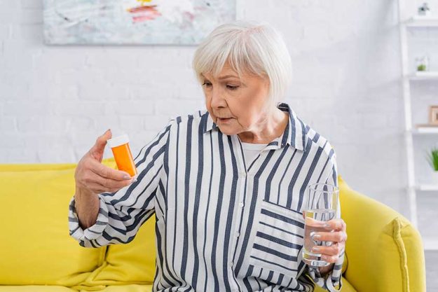 senior woman looking jar pills holding glass water home