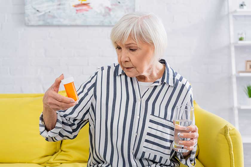 senior woman looking jar pills holding glass water home