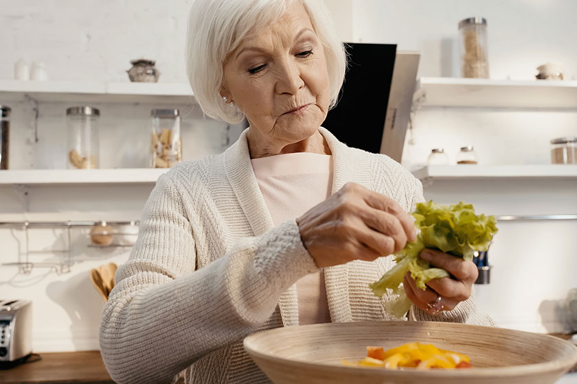 senior woman preparing vegetable salad adding fresh lettuce bowl senior woman preparing vegetable salad adding fresh lettuce bowl