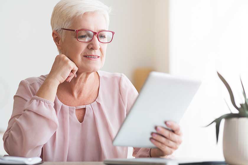 smiling senior woman with glasses reading book on digital tablet smiling senior woman with glasses reading book on digital tablet