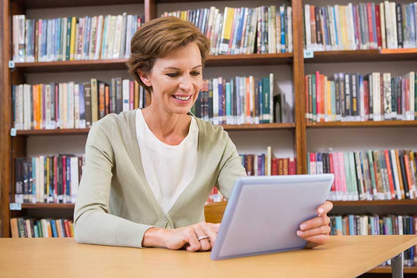 smiling teacher using tablet pc at library 1