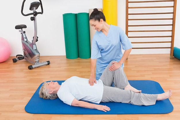 therapist working with senior woman on exercise mat