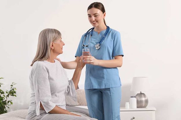 young healthcare worker giving glass water senior woman indoors
