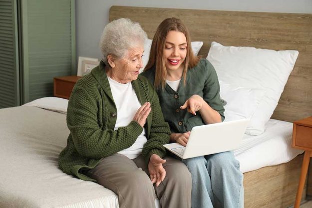 young woman her grandmother using laptop bedroom