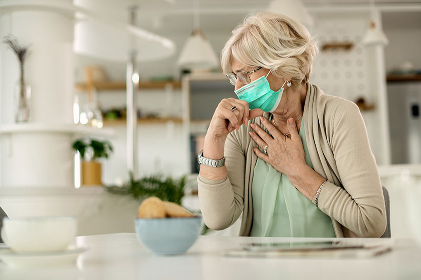 senior woman feeling chest pain coughing while wearing face mask