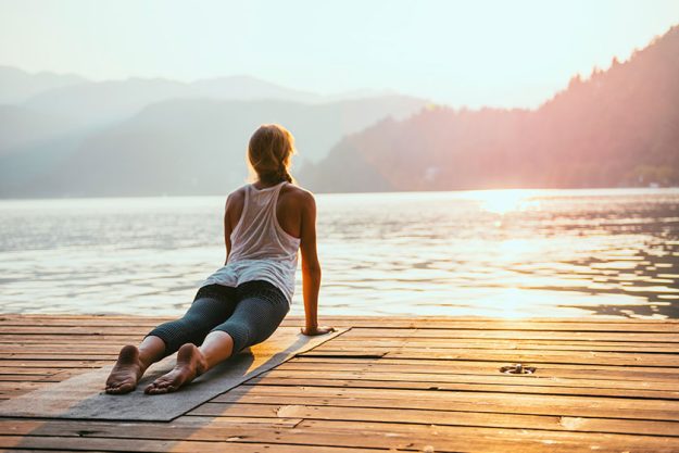 woman practicing yoga by the lake