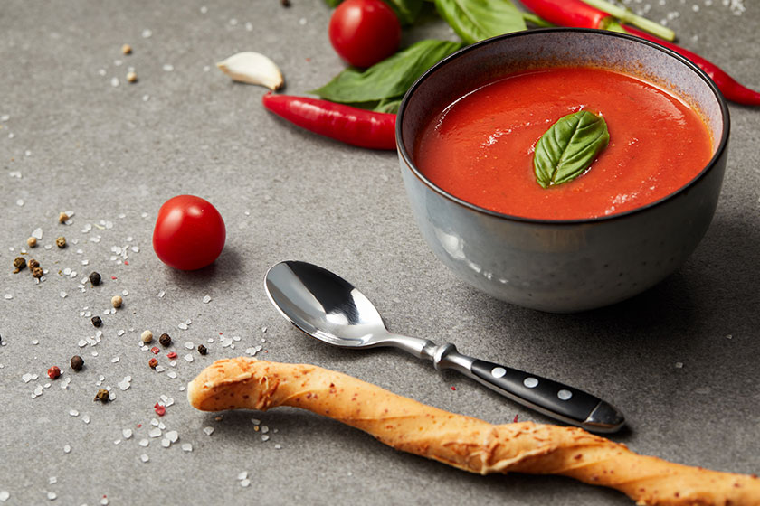 cooked tomato soup chili peppers basil bread stick grey table cooked tomato soup chili peppers basil bread stick grey table