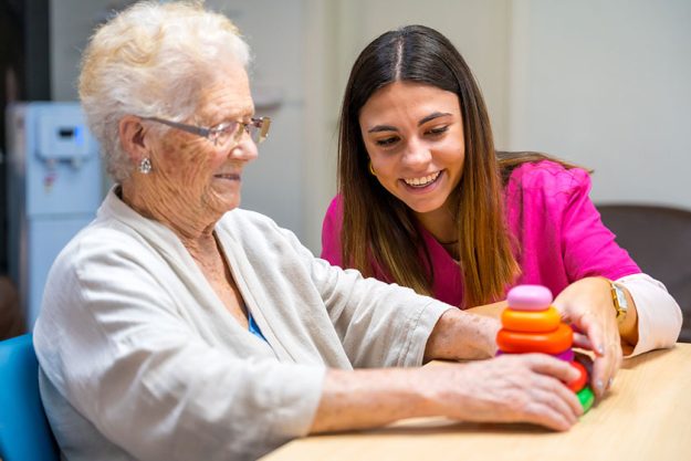 cute nurse helping woman play board skill game nursing home