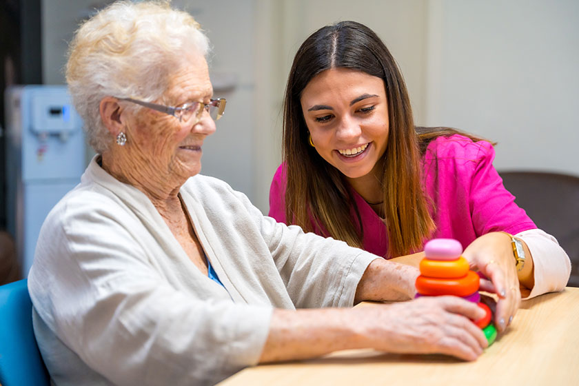 cute nurse helping woman play board skill game nursing home