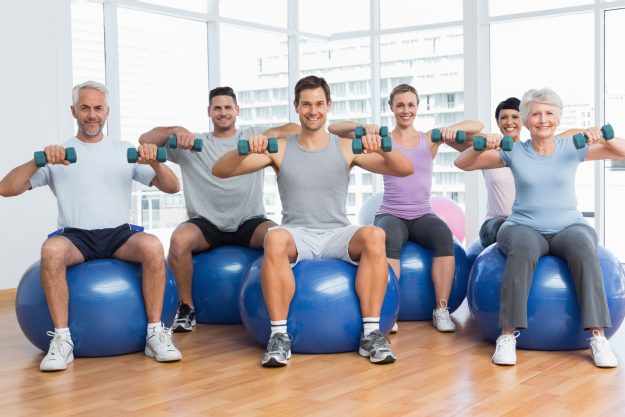 fitness class with dumbbells sitting on exercise balls in gym scaled