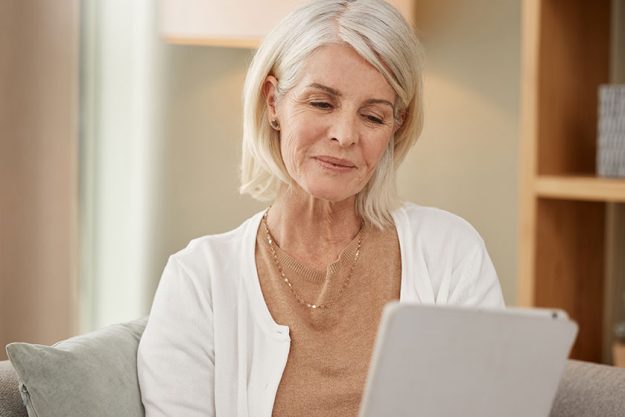 a mature woman using a digital tablet on the sofa