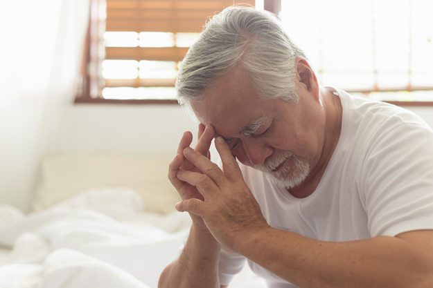asian elderly man headache sitting bed morning 