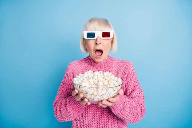 photo portrait of terrified old woman watching horror film holding popcorn bowl isolated on pastel