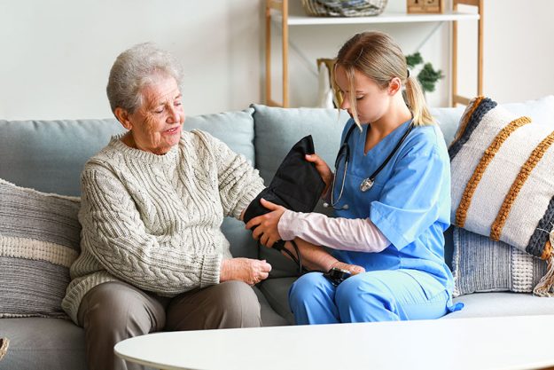 young caregiver measuring blood pressure senior woman home