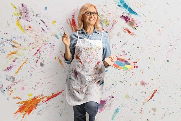 happy middle aged woman leaning wall paint holding brush palette