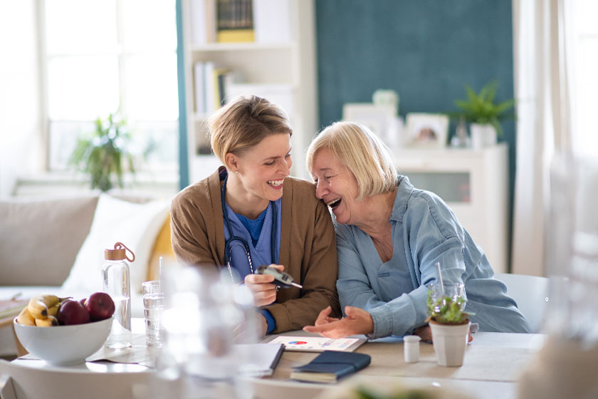 healthcare worker with laughing senior woman patient measuring blood glucose indoors