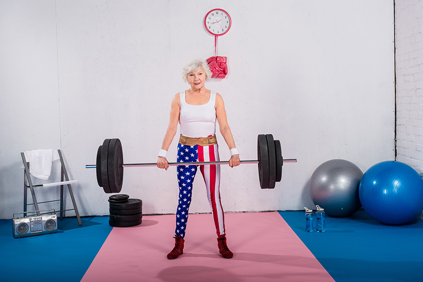 patriotic senior sportswoman lifting barbell smiling camera
