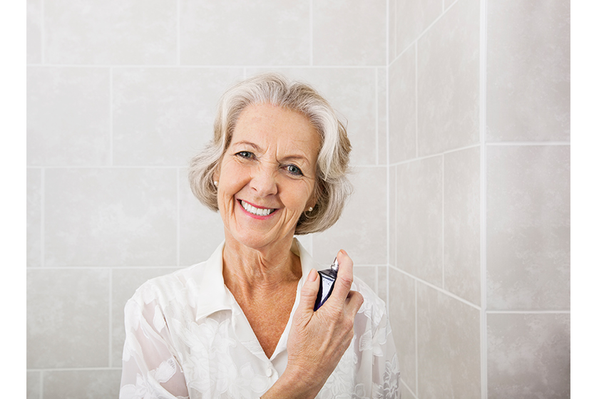 portrait happy senior woman spraying perfume bathroom