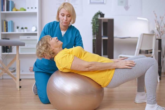 rehabilitation doctor helps patient train her back fitball physical medicine