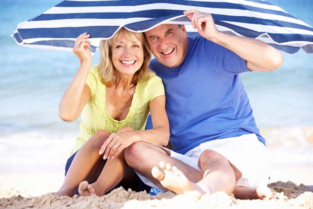 senior couple sheltering from sun under beach umbrella