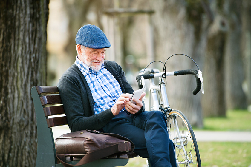 senior man with bicycle in town holding smart phone texting