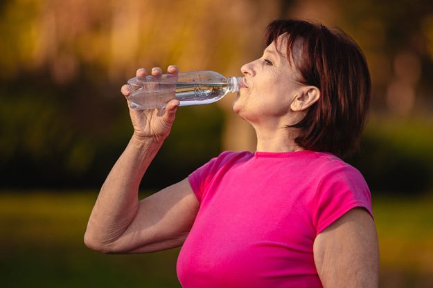 elderly woman drinking water from a bottle at sunset elderly woman drinking water from a bottle at sunset