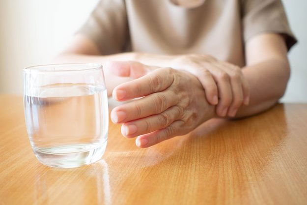 elderly woman hands tremor symptom reaching out glass water wood elderly woman hands tremor symptom reaching out glass water wood