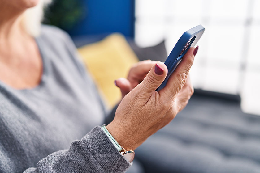 middle age blonde woman using smartphone sitting sofa home