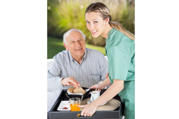 portrait of smiling female nurse serving breakfast to senior man