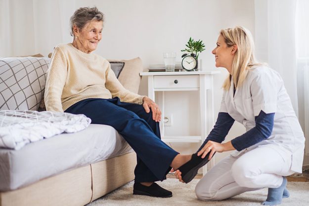 a health visitor putting on slippers on a senior woman at home at christmas time