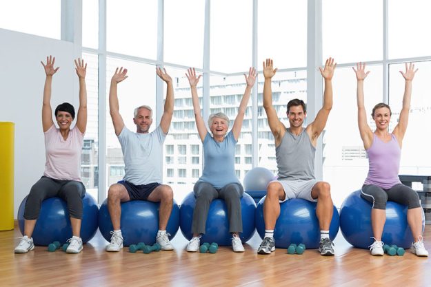 class sitting on exercise balls and raising hands in gym