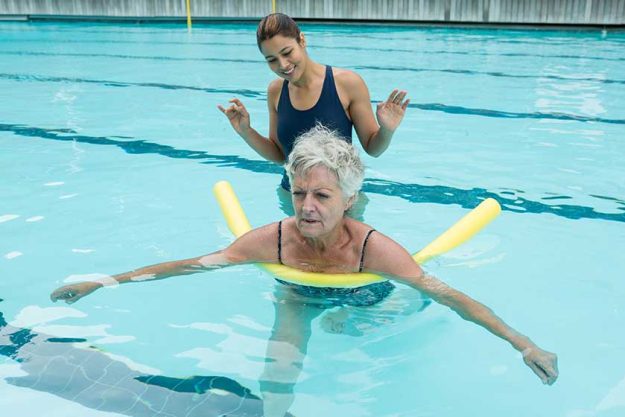 female coach helping senior woman in pool